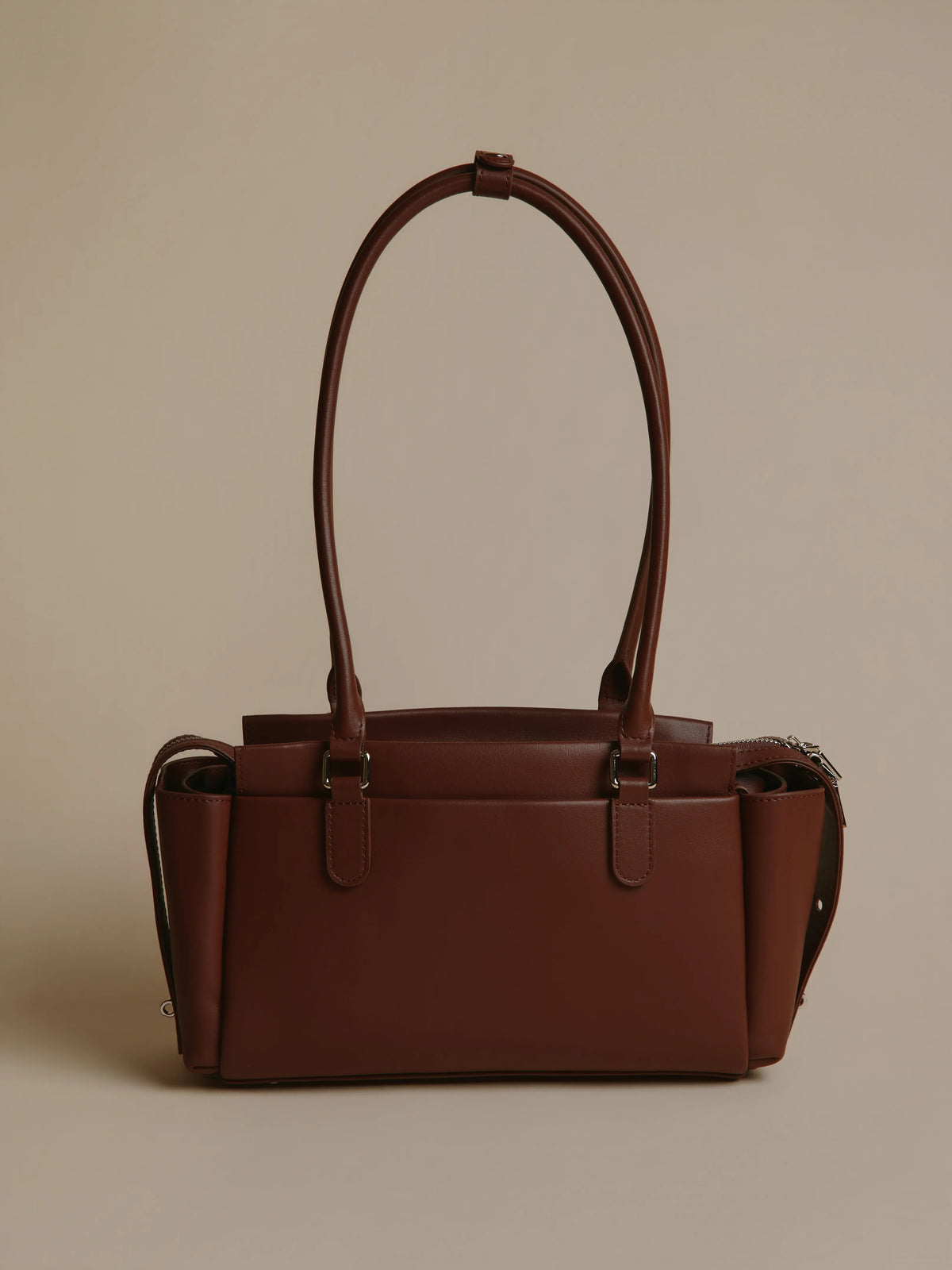 Brown handbag with a smooth surface and long handles.