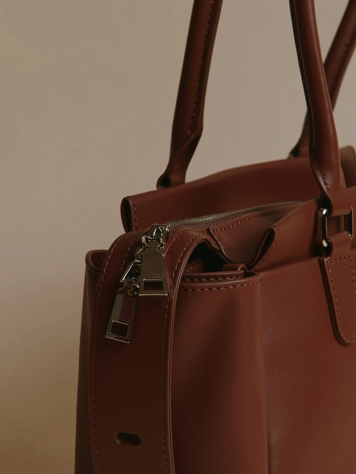 Close-up shot of a brown handbag showing zipper and handles.